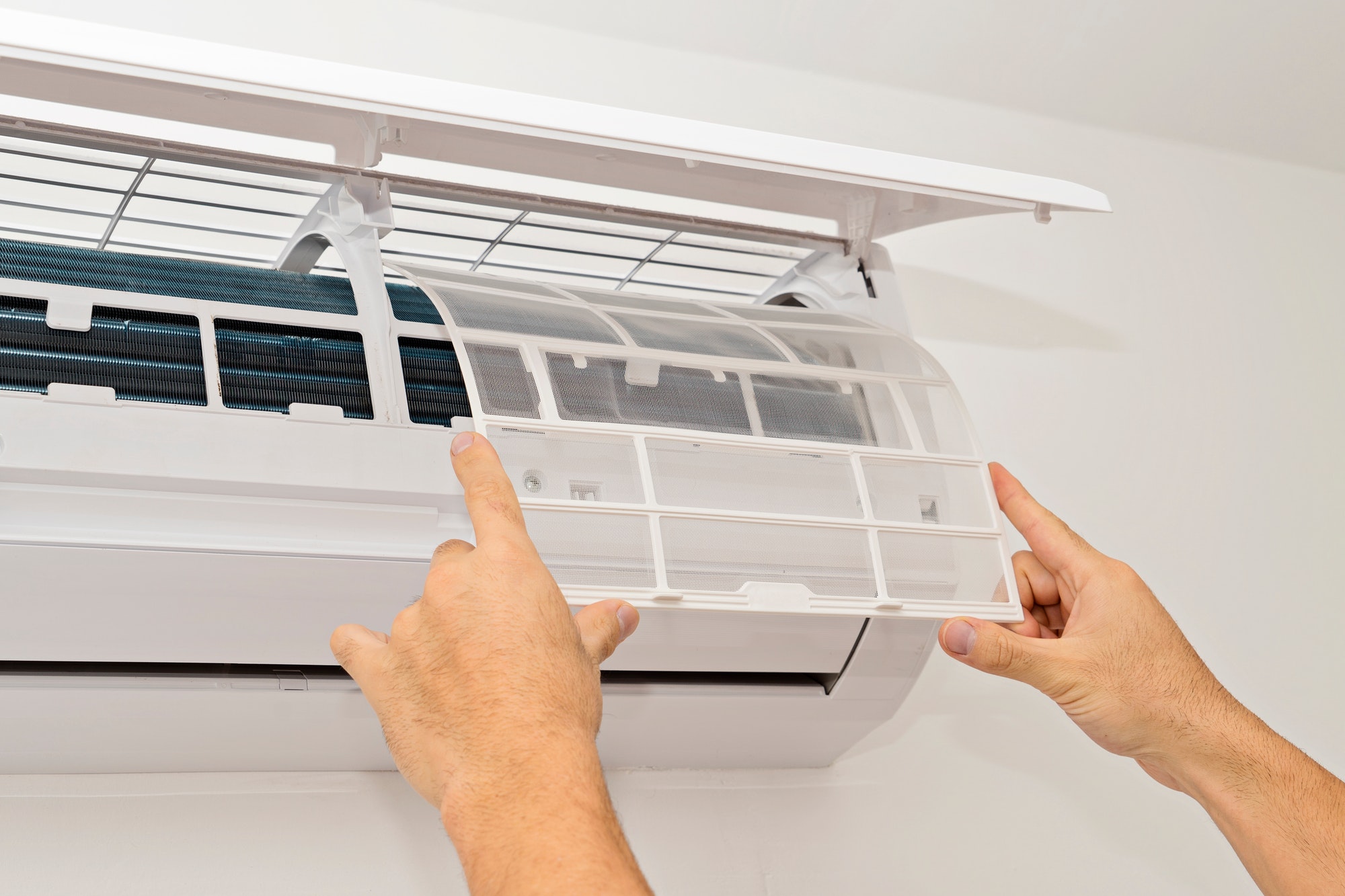 changing-the-filter-of-the-air-conditioner.jpg Person changing the air filter on a wall-mounted ductless mini split system, performing routine HVAC maintenance for improved indoor air quality and efficiency.